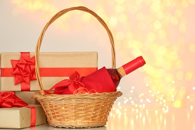 Wicker basket with bottle of wine and gift boxes against blurred lights