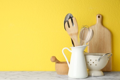 Photo of Different kitchen utensils on marble table against yellow background. Space for text