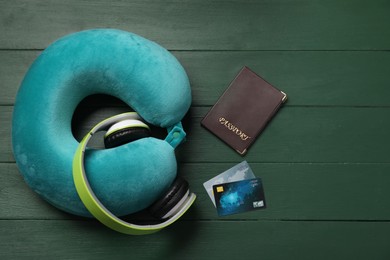 Photo of Turquoise travel pillow, passport and credit cards on green wooden background, flat lay. Space for text