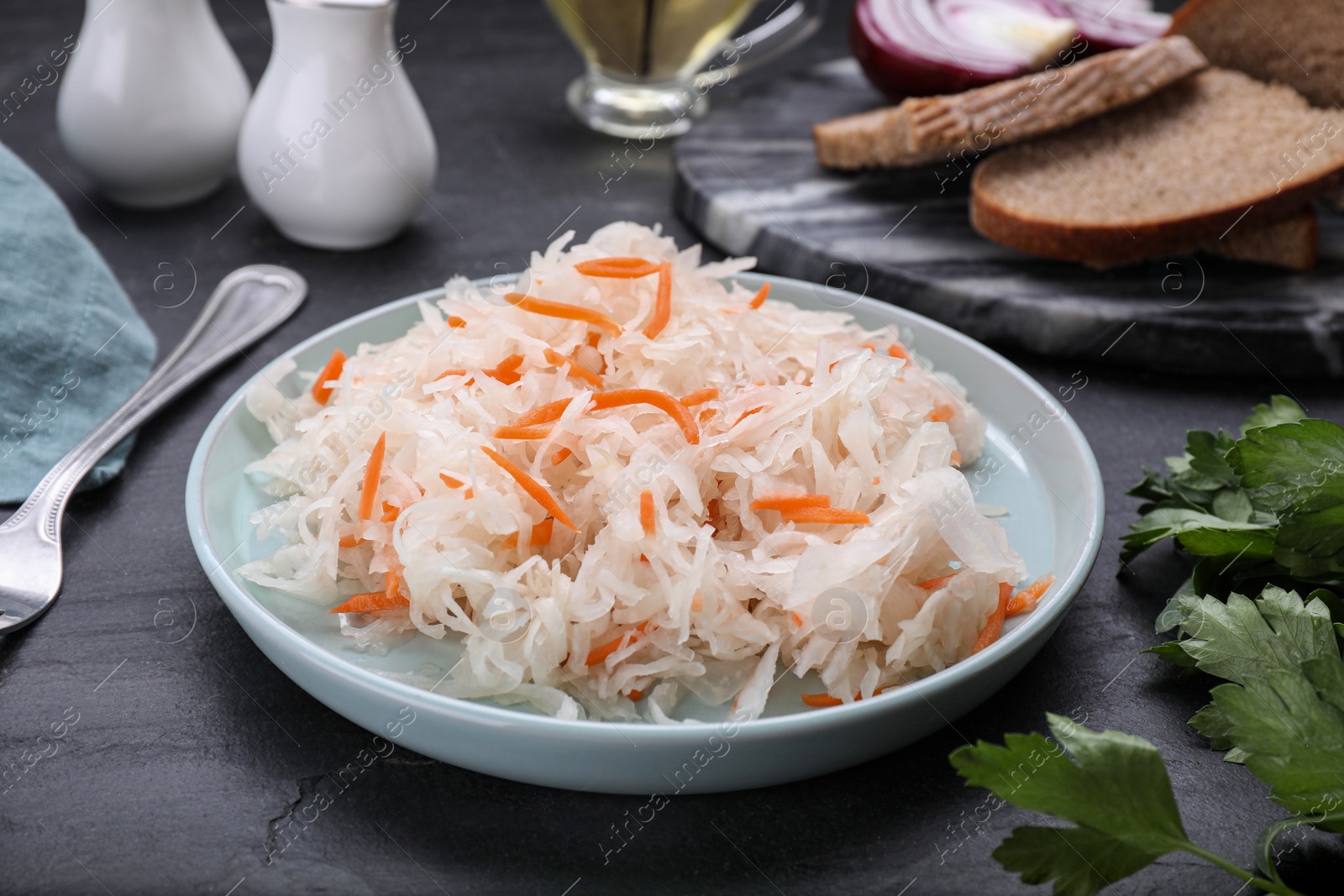 Photo of Plate of tasty sauerkraut and ingredients on black table