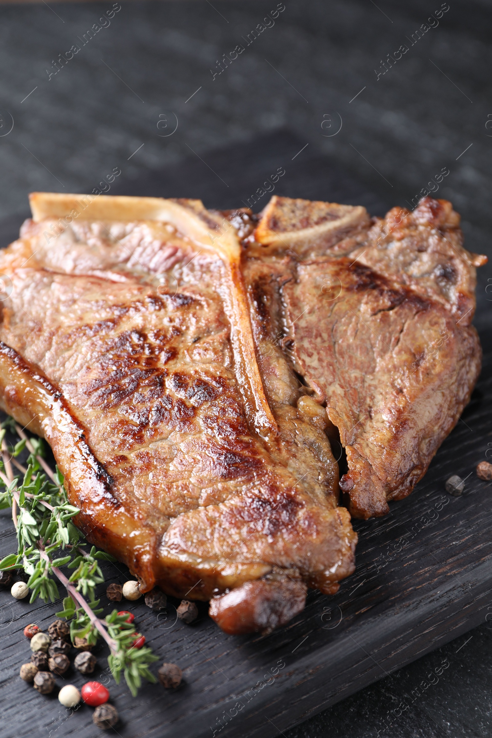 Photo of Delicious fried beef meat, thyme and peppercorns on table, closeup