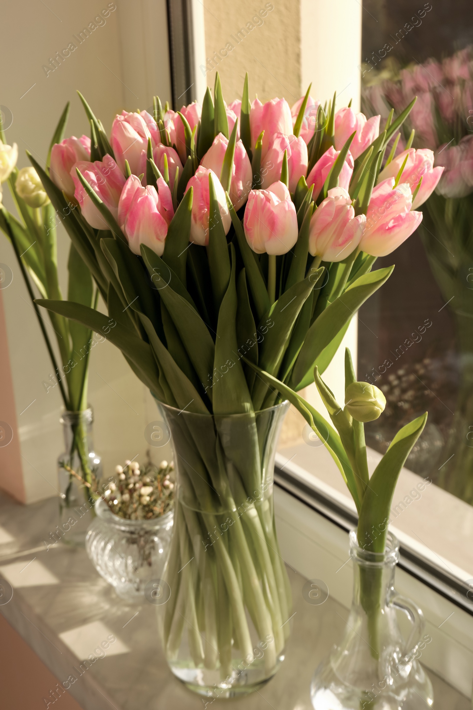 Photo of Bouquet of beautiful tulips in glass vase and spring flowers on windowsill indoors