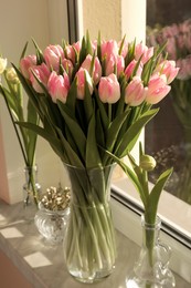Bouquet of beautiful tulips in glass vase and spring flowers on windowsill indoors