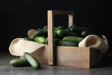 Photo of Wooden basket full of fresh ripe cucumbers on dark grey table