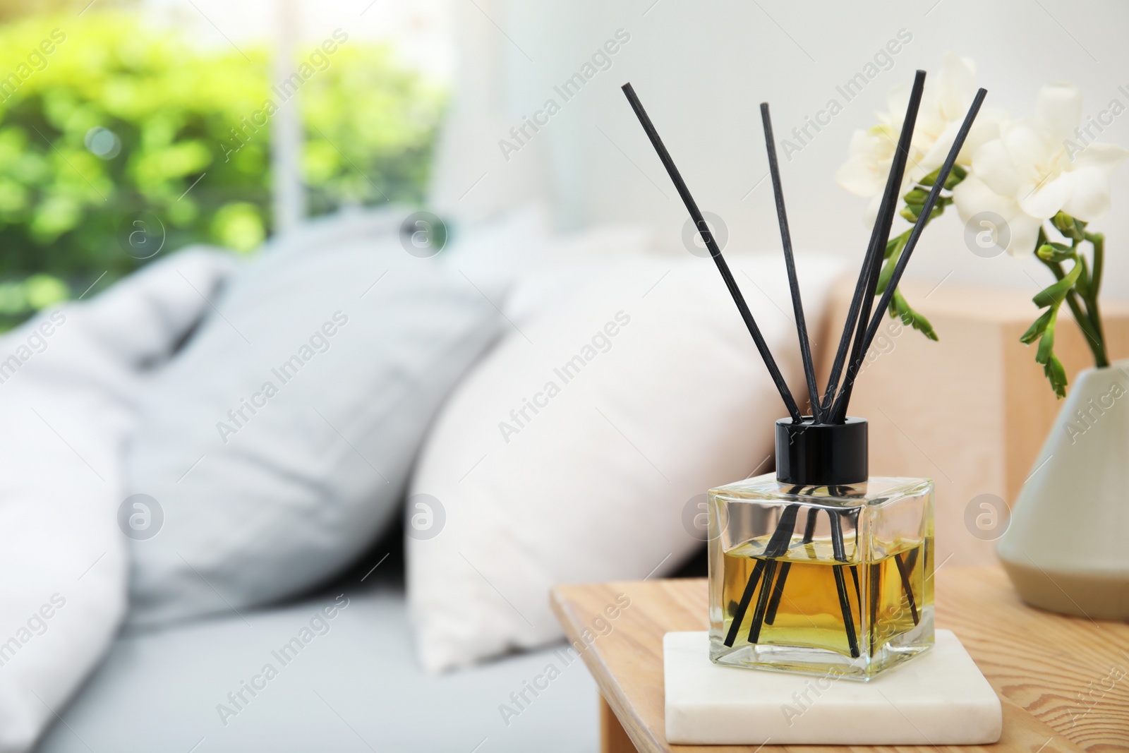 Photo of Reed diffuser and vase with bouquet on wooden nightstand in bedroom. Space for text