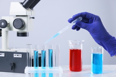 Scientist dripping liquid from pipette into test tube at table, closeup