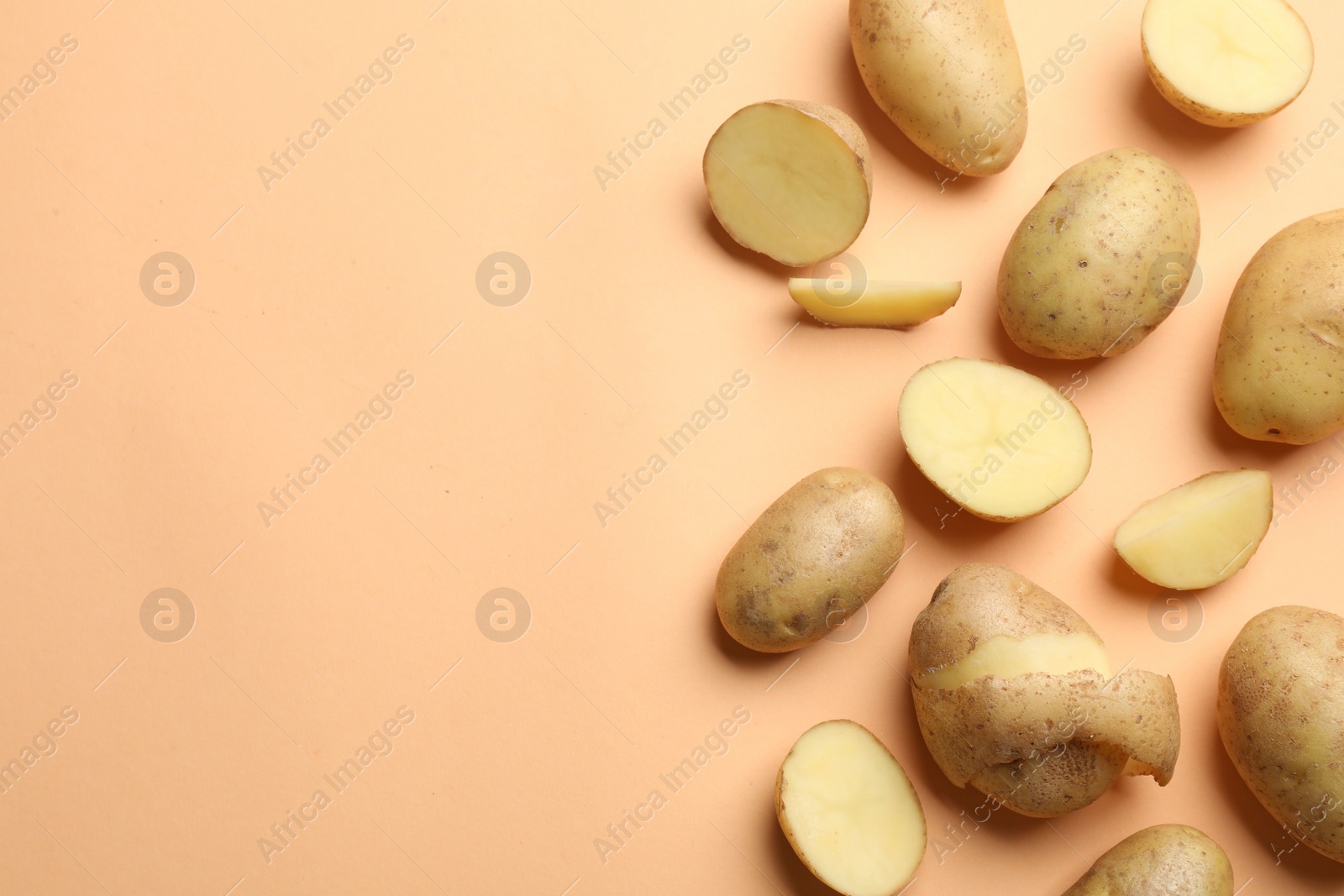 Photo of Fresh raw potatoes on pale orange background, flat lay. Space for text