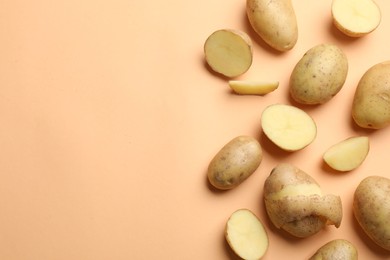 Photo of Fresh raw potatoes on pale orange background, flat lay. Space for text