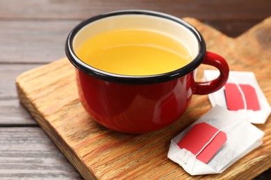 Tea bags and cup of hot beverage on wooden table, closeup