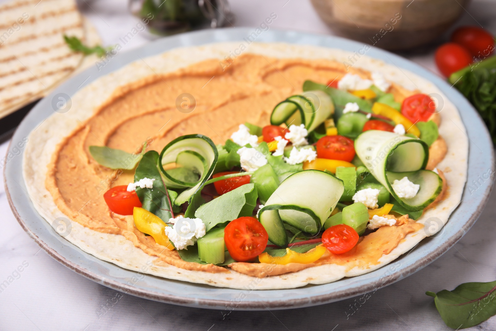 Photo of Tortilla with hummus and vegetables on table, closeup