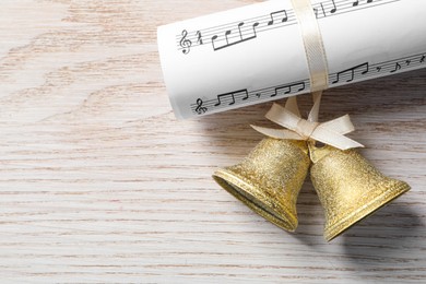 Photo of Golden shiny bells with bow and music sheet on wooden table, flat lay. Space for text. Christmas decoration