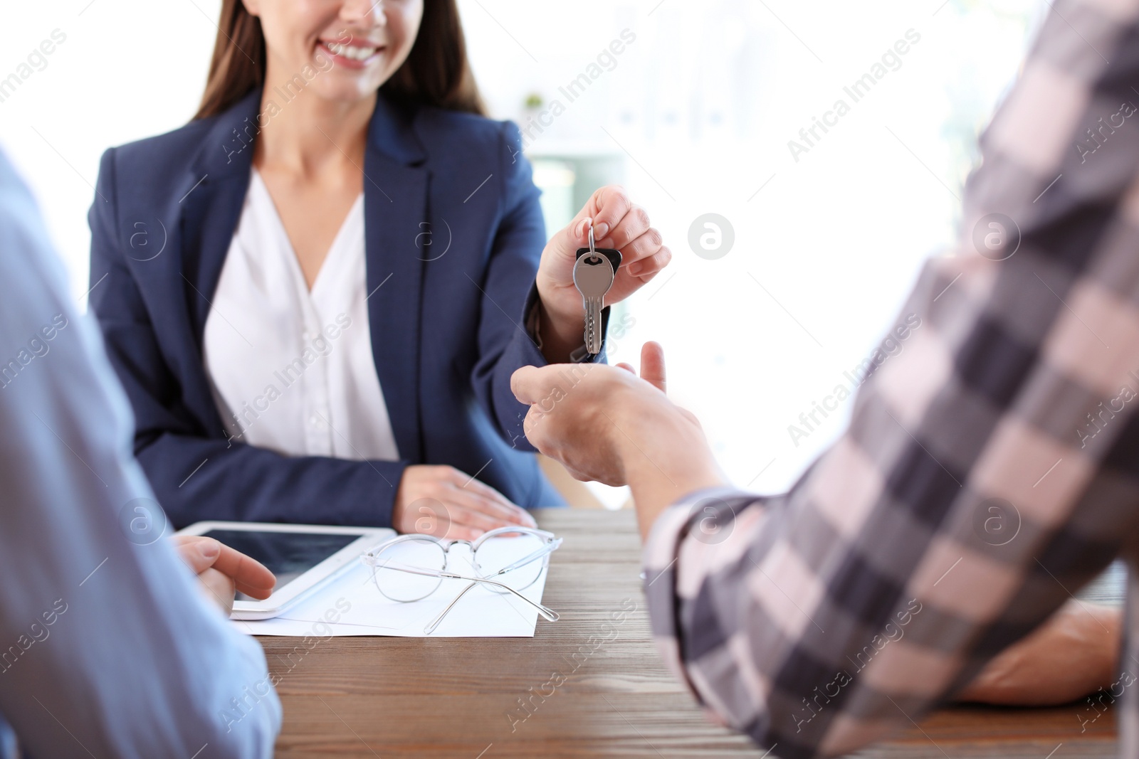 Photo of Female real estate agent giving house key to couple at table in office