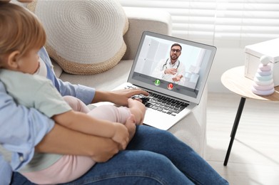 Mother and daughter having online consultation with pediatrician via laptop on sofa at home