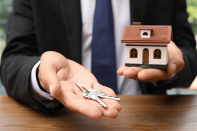 Photo of Real estate agent holding house model and keys at table