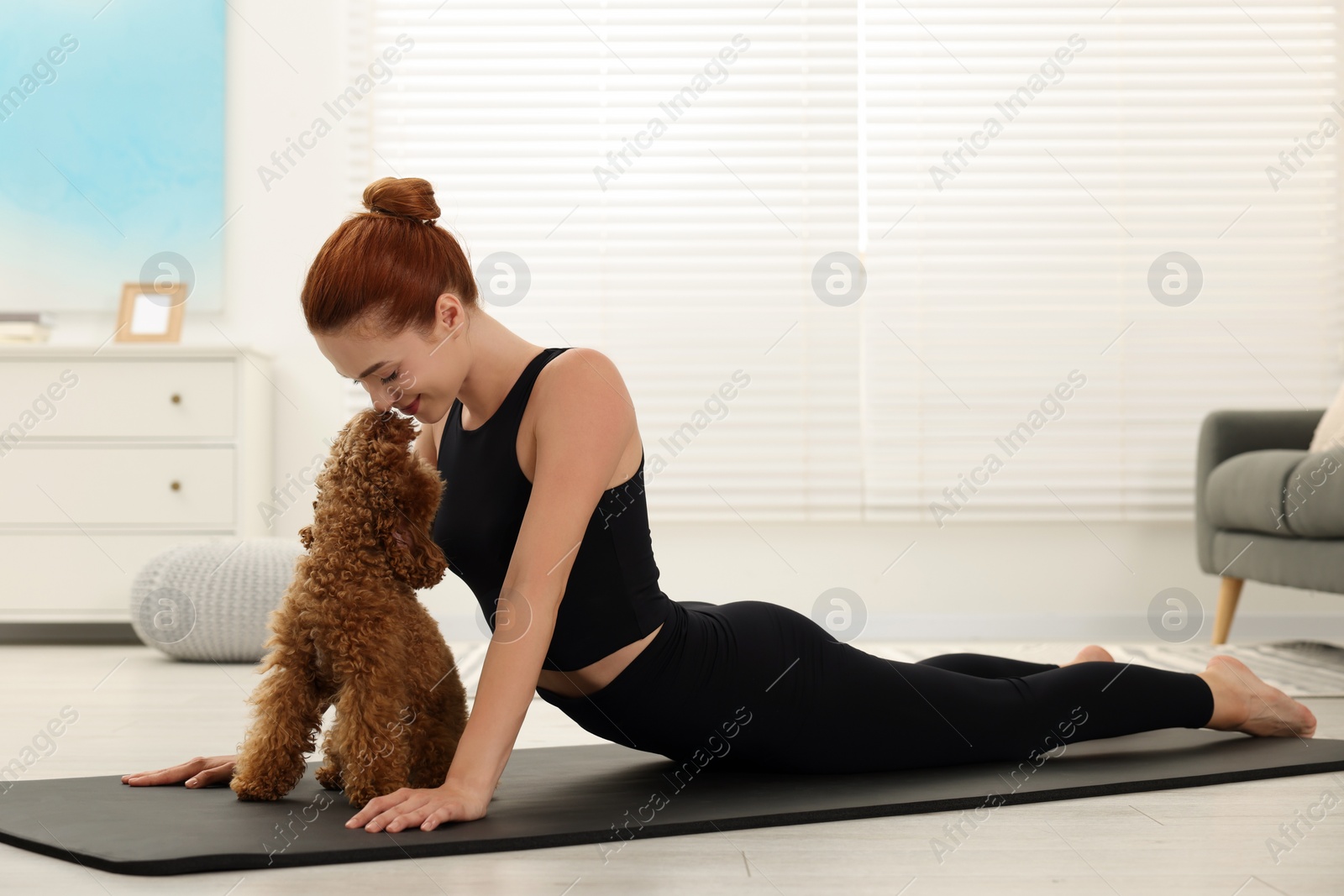 Photo of Young woman practicing yoga on mat with her cute dog at home