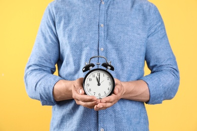 Young man holding clock on color background. Time management