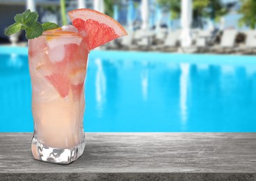 Fresh alcoholic Grapefruit Mojito cocktail on wooden table near outdoor swimming pool, space for text