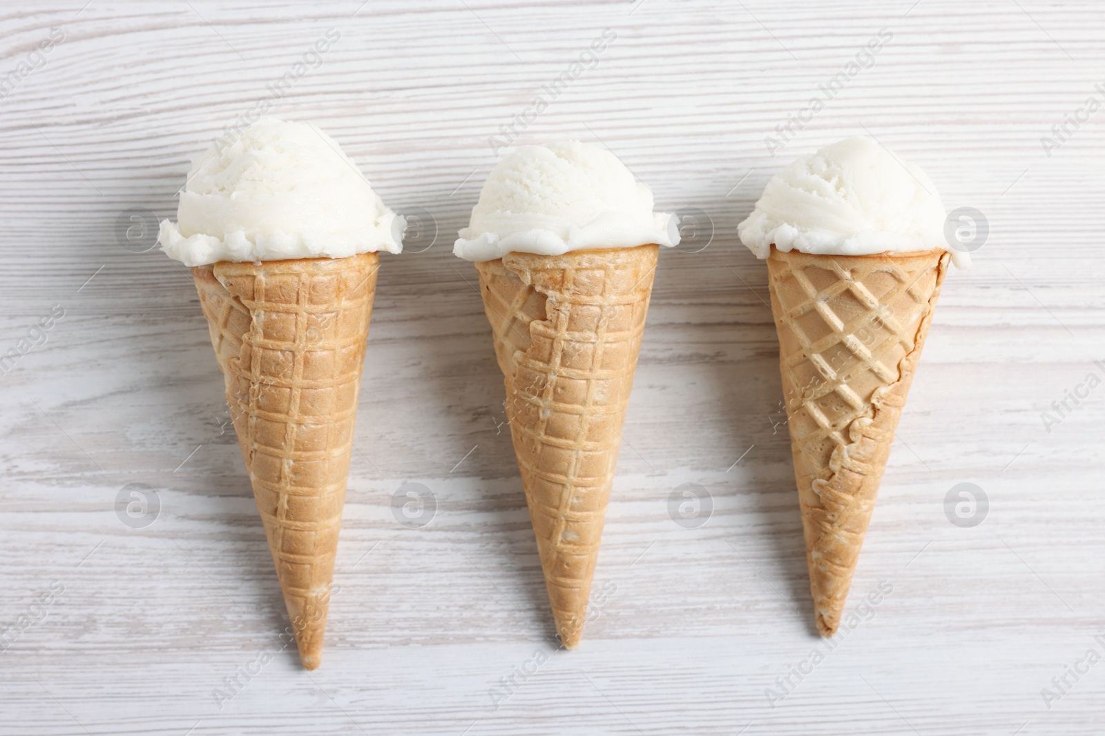 Photo of Ice cream scoops in wafer cones on light wooden table, flat lay