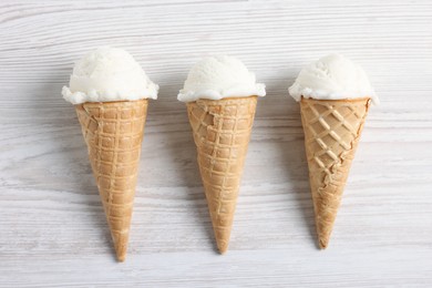 Ice cream scoops in wafer cones on light wooden table, flat lay