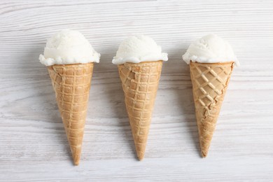 Photo of Ice cream scoops in wafer cones on light wooden table, flat lay