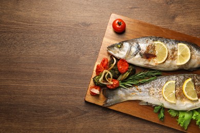 Photo of Delicious baked fish and vegetables on wooden table, top view. Space for text