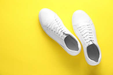 Pair of stylish white sneakers on yellow background, top view. Space for text