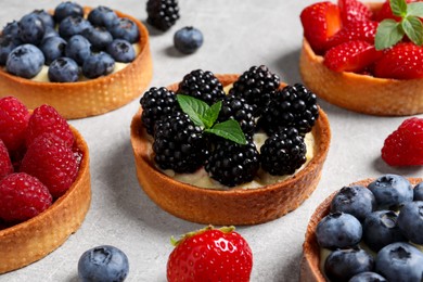 Photo of Tartlets with different fresh berries on light table. Delicious dessert