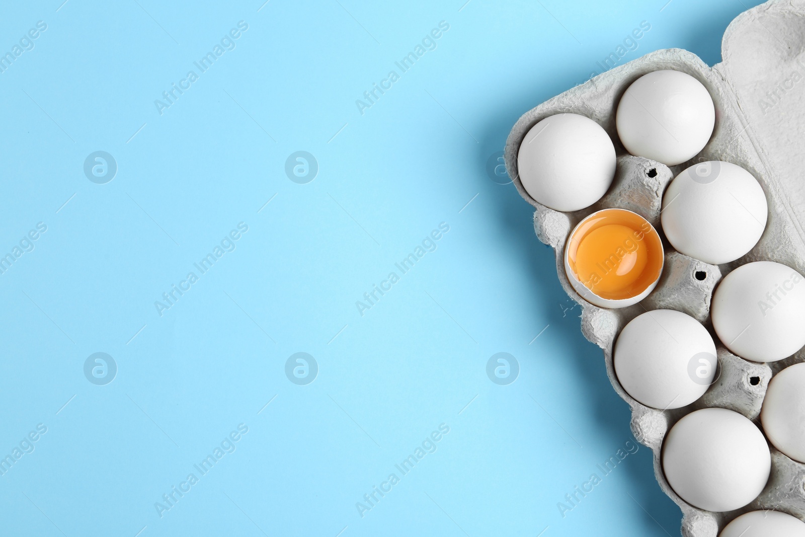 Photo of Fresh chicken eggs in box on light blue background, top view. Space for text