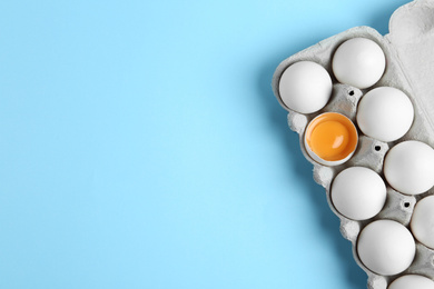 Photo of Fresh chicken eggs in box on light blue background, top view. Space for text