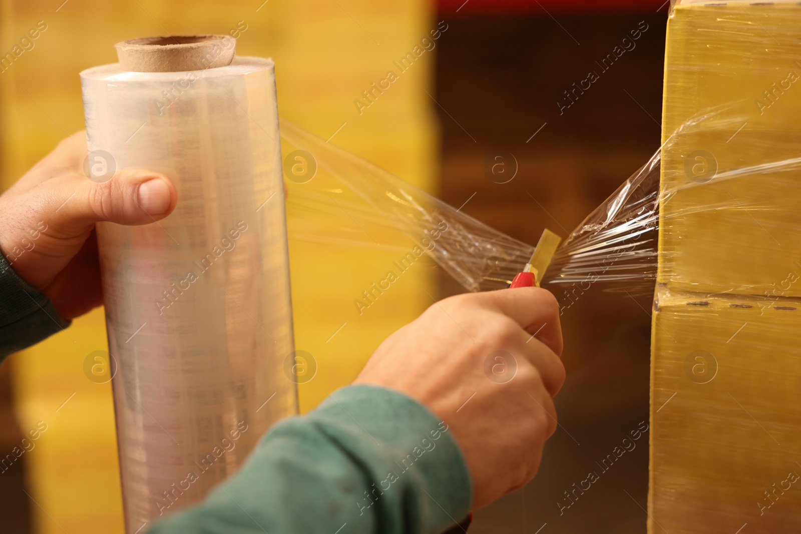 Photo of Worker wrapping boxes in stretch film at warehouse, closeup