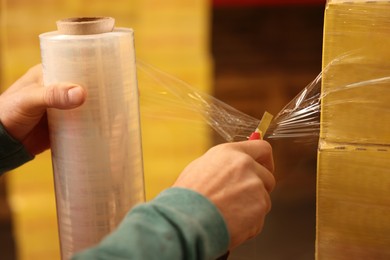 Worker wrapping boxes in stretch film at warehouse, closeup