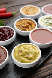 Photo of Different tasty sauces in bowls on wooden table, closeup