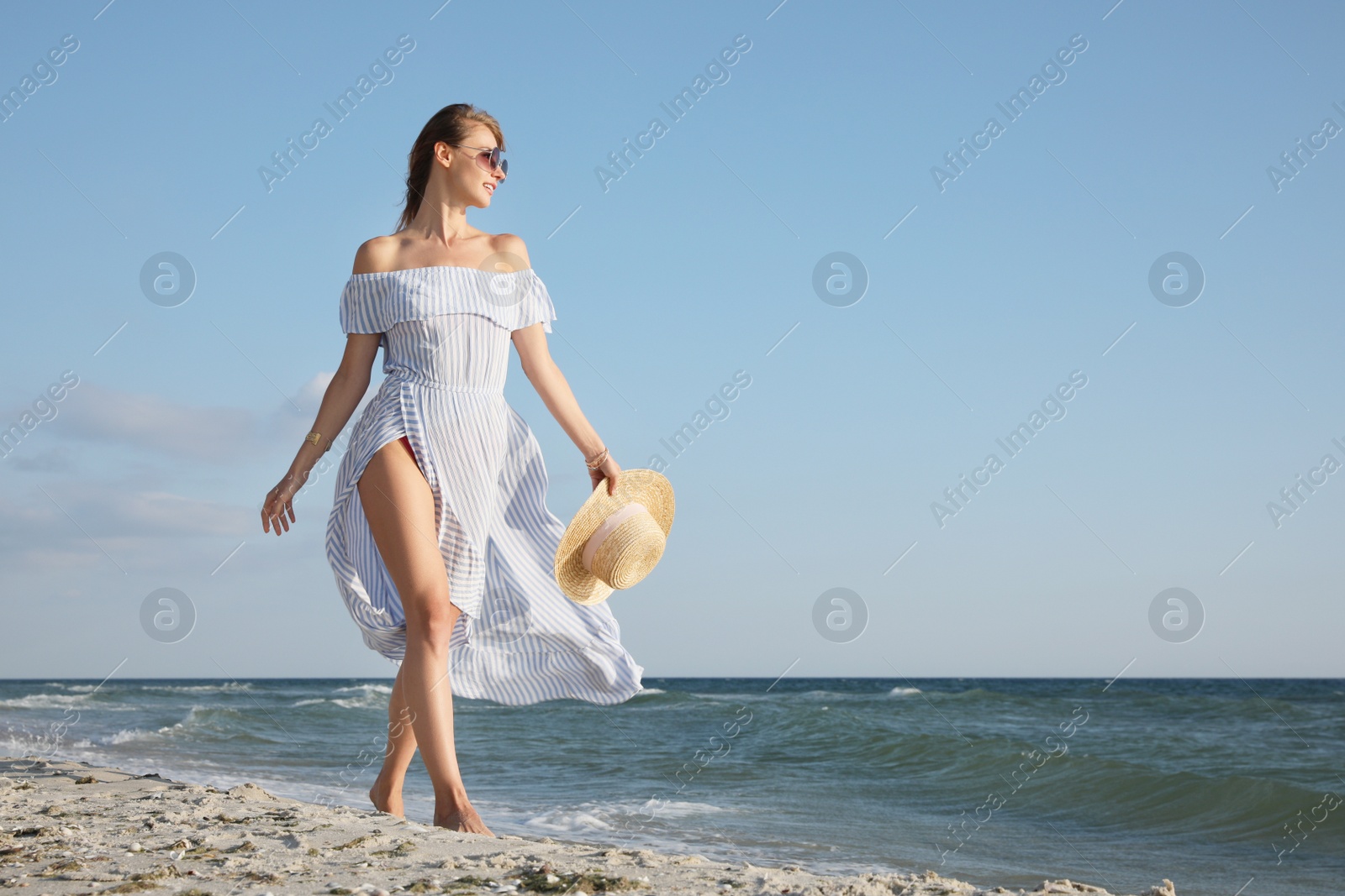 Photo of Woman in dress with straw hat walking by sea on sunny day