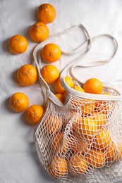 Photo of Net bag with many fresh ripe tangerines on white cloth, flat lay