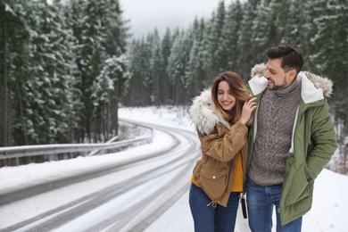 Couple walking near snowy forest, space for text. Winter vacation