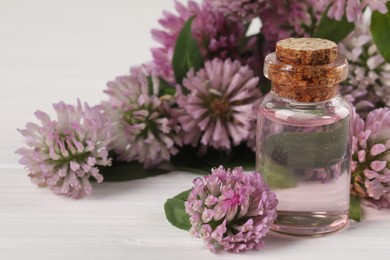 Photo of Beautiful clover flowers and essential oil on white wooden table, closeup. Space for text