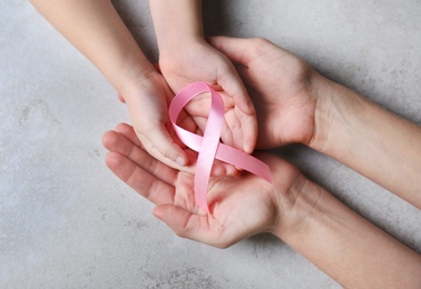 Woman and girl holding pink ribbon on grey background, top view. Breast cancer awareness