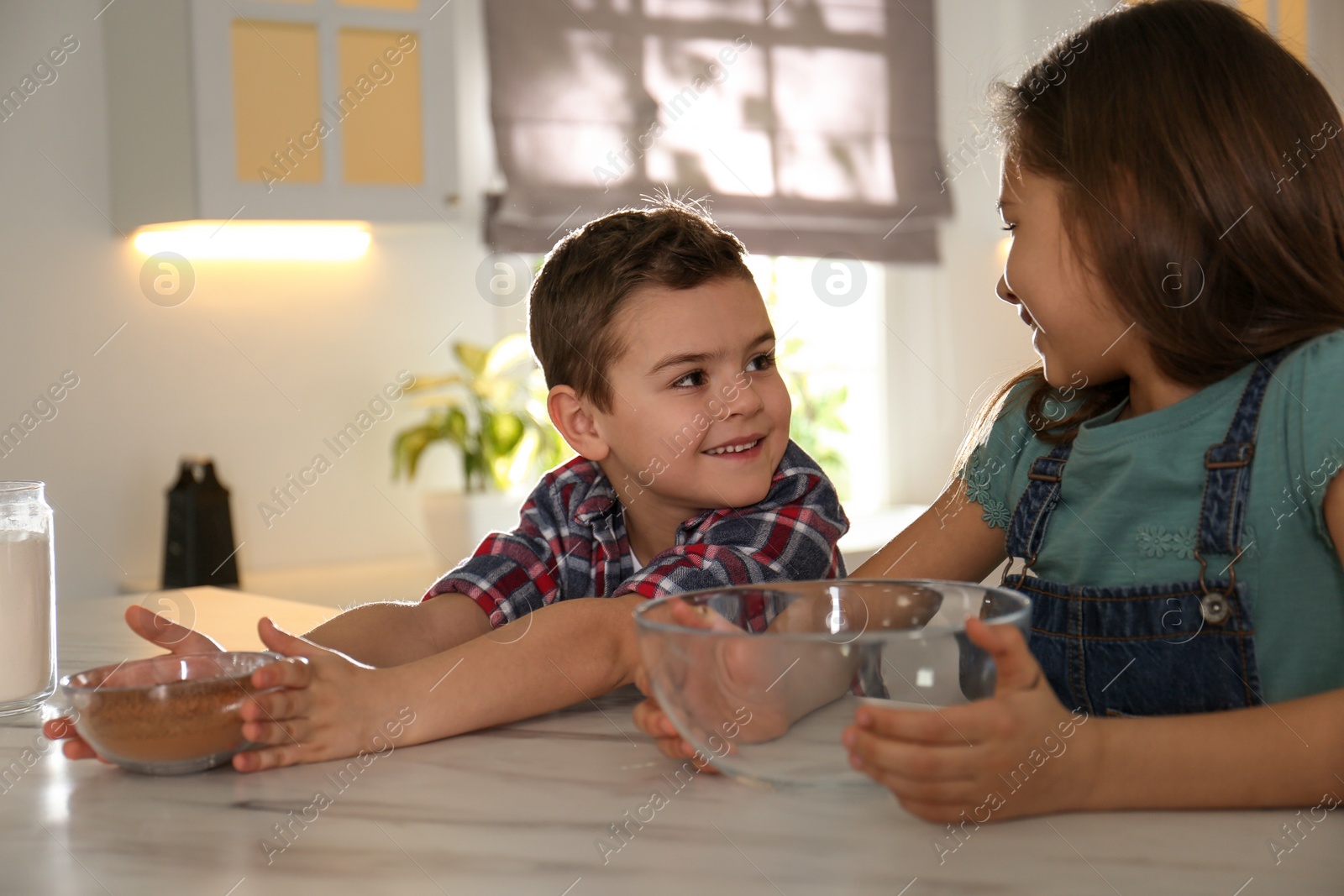 Photo of Cute little children at table with cooking ingredients in kitchen