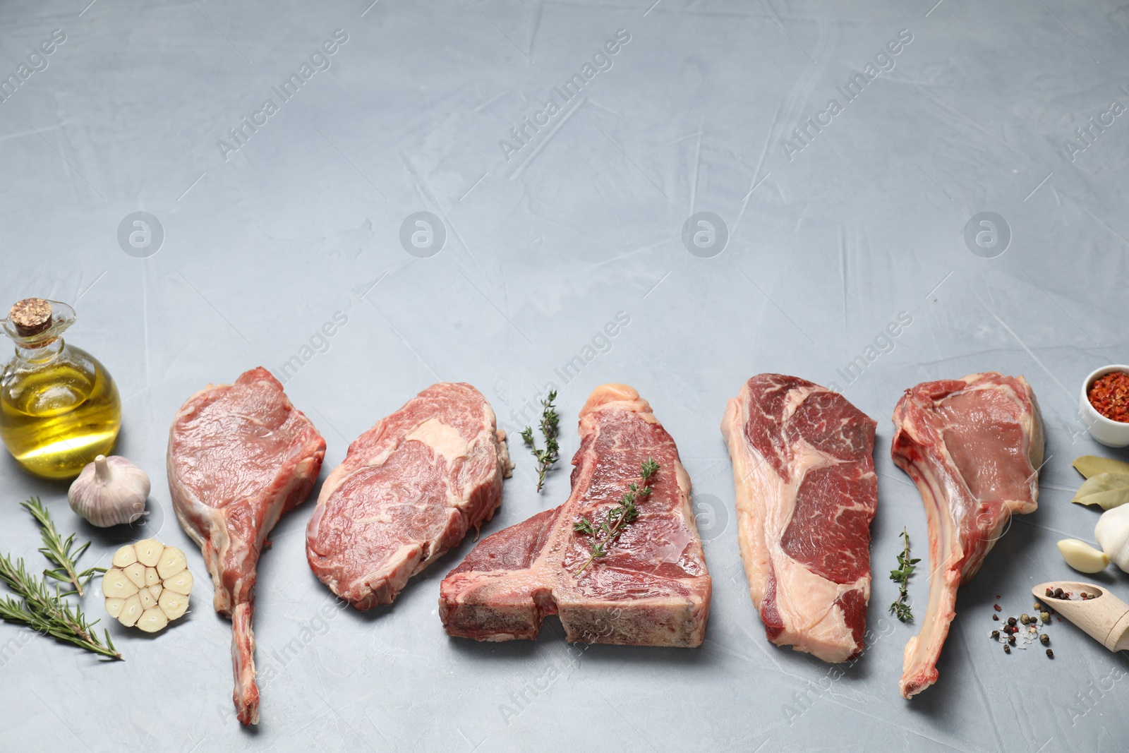 Photo of Fresh raw beef cuts, spices and oil on light grey textured table, above view. Space for text