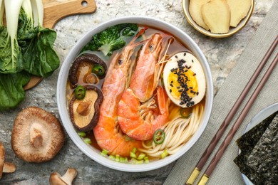 Photo of Delicious ramen with shrimps, ingredients and chopsticks on grey textured table, flat lay. Noodle soup