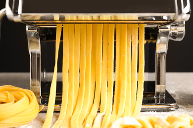 Pasta maker machine with dough on grey table, closeup