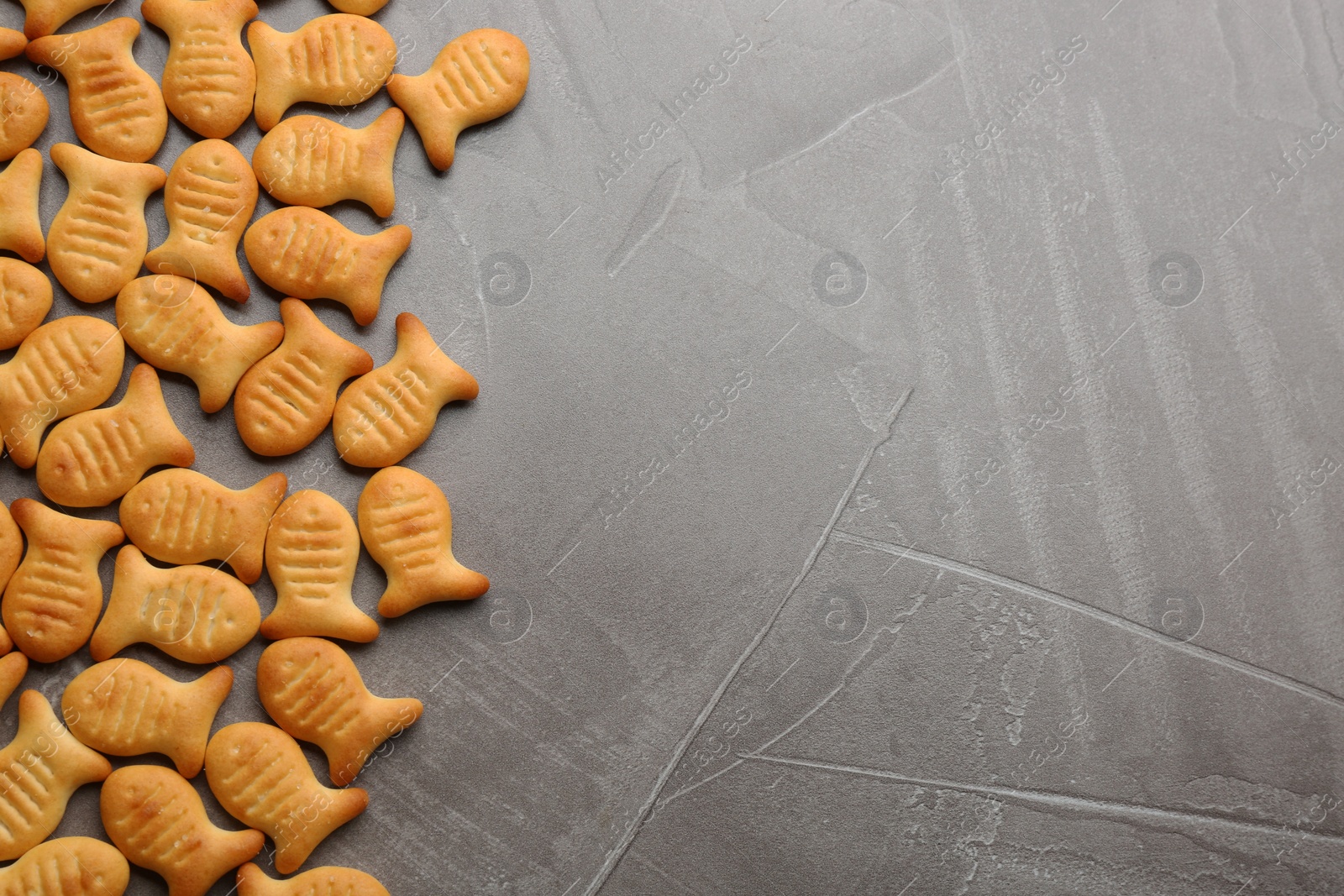 Photo of Delicious goldfish crackers on grey table, flat lay. Space for text