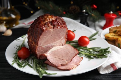 Photo of Plate with delicious ham, tomatoes and rosemary on black wooden table