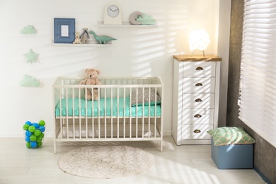 Photo of Cute nursery interior with comfortable crib near white wall