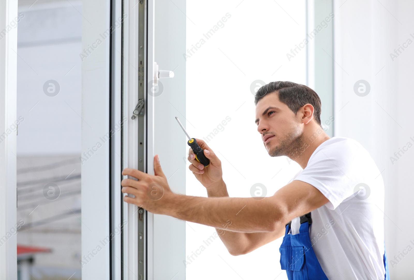 Photo of Construction worker repairing plastic window with screwdriver indoors