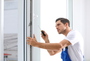 Construction worker repairing plastic window with screwdriver indoors