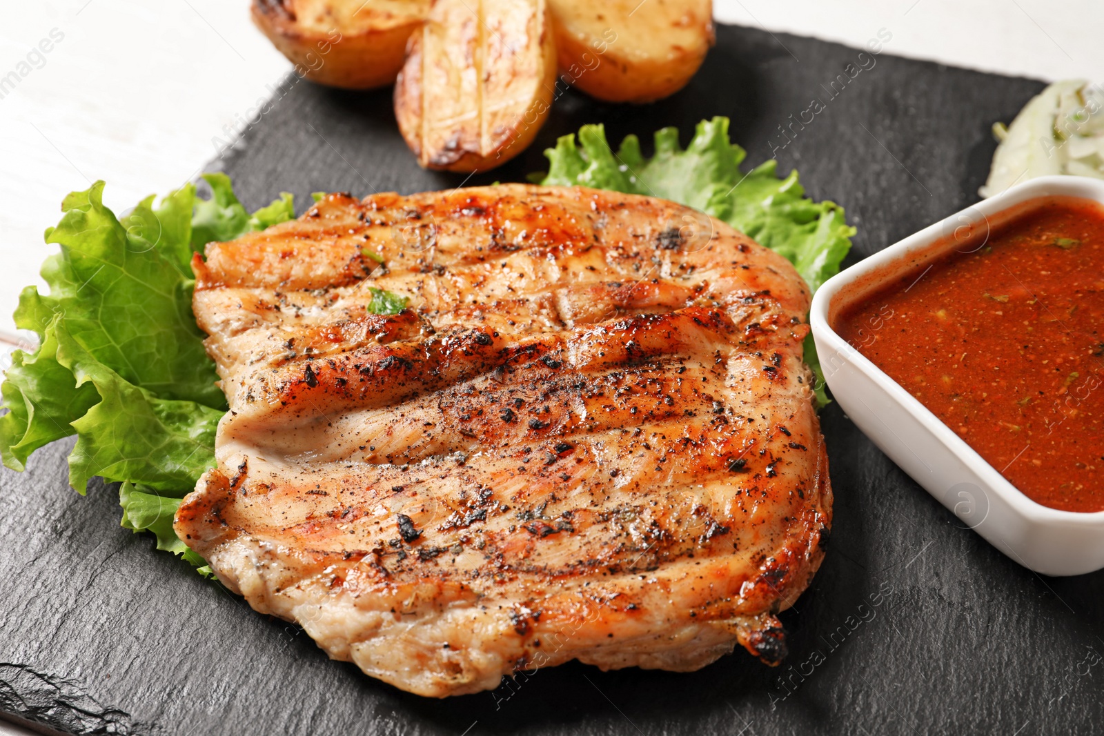 Photo of Tasty grilled meat and sauce served on slate plate, closeup