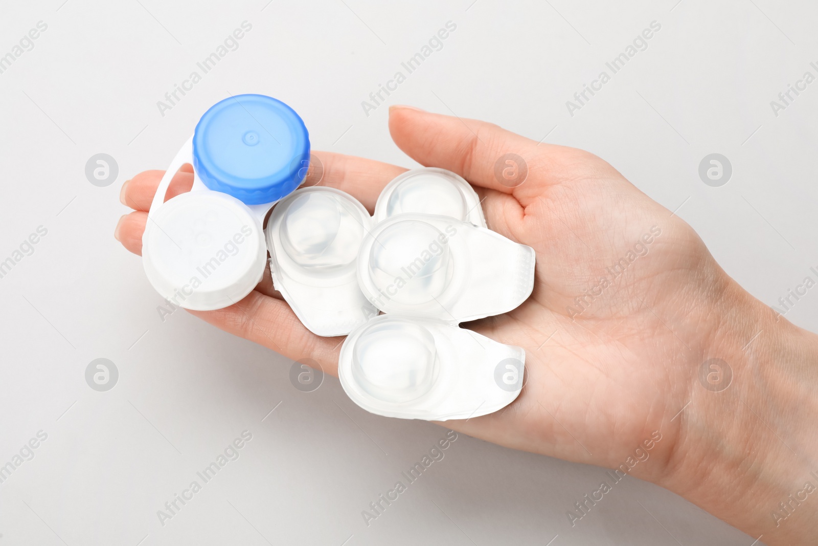 Photo of Woman holding packages with contact lenses and case on white background, top view