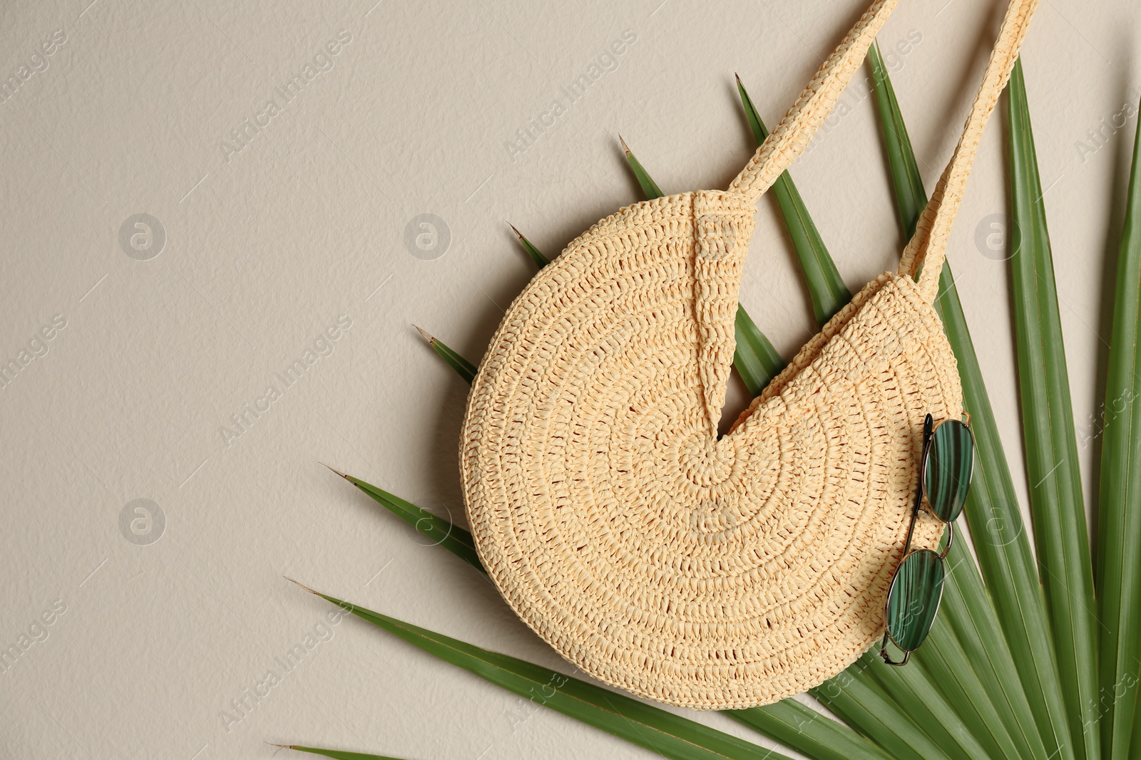 Photo of Elegant woman's straw bag with tropical leaf and sunglasses on beige background, top view. Space for text