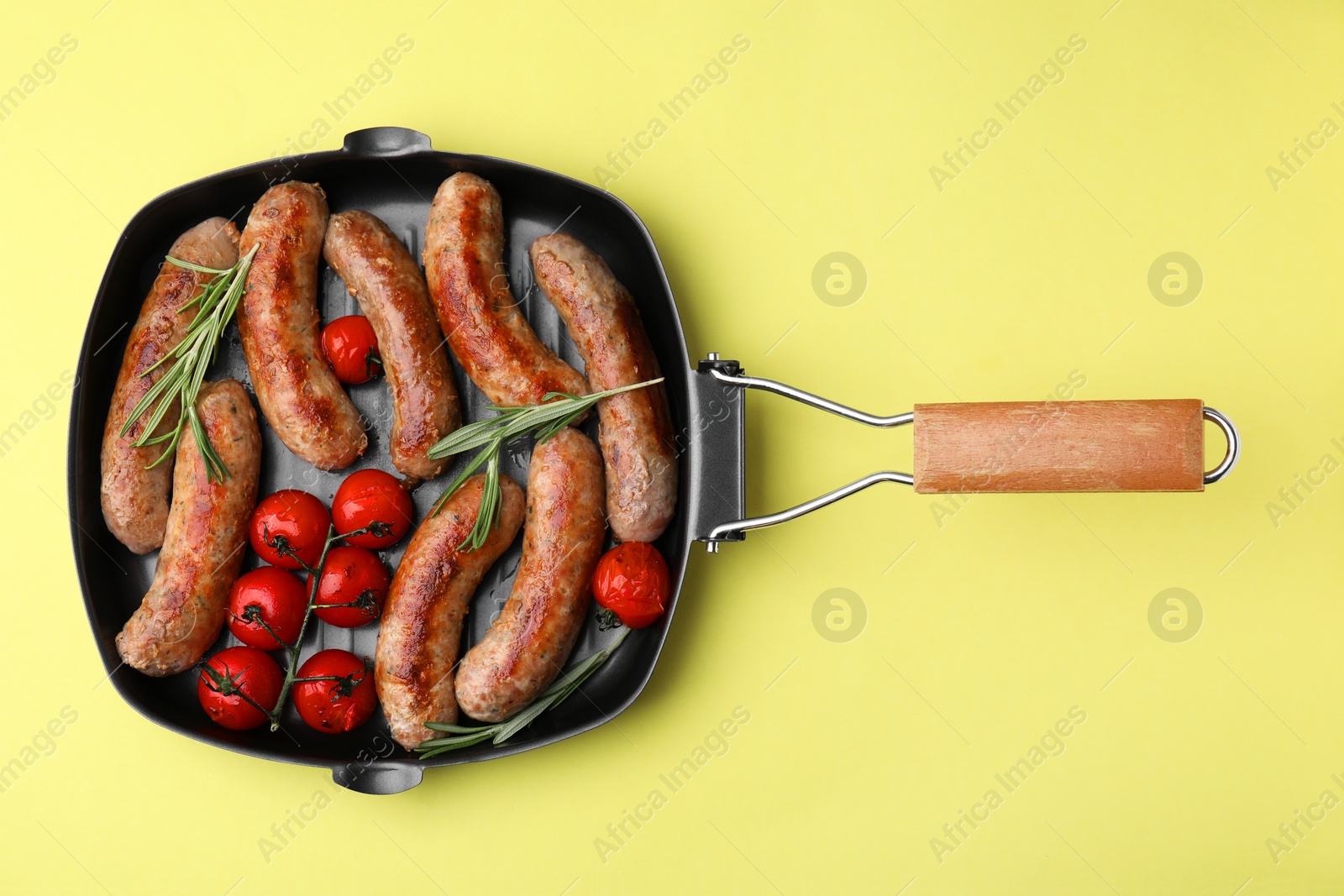 Photo of Grill pan with tasty homemade sausages, rosemary and tomatoes on yellow table, top view